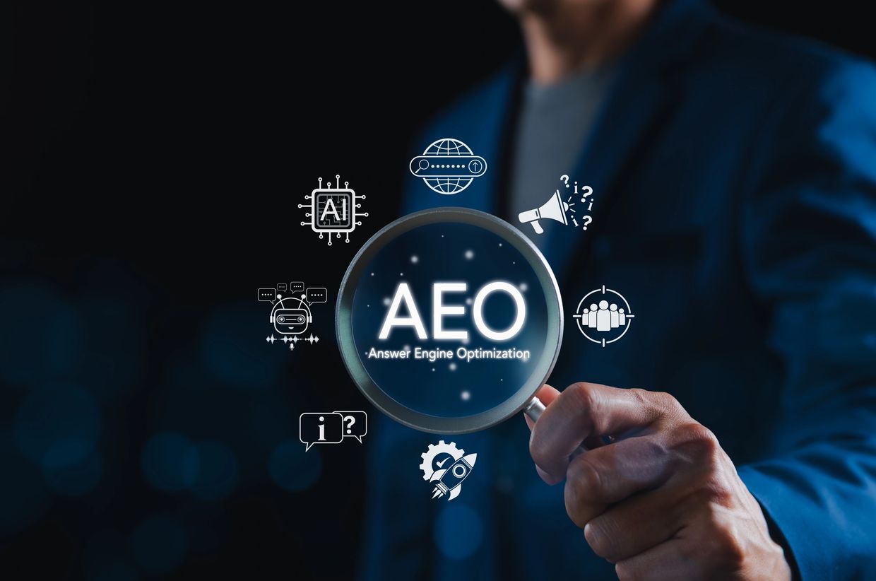 Acronym AEO. Answer Engine Optimization is written below it. AI emojis surround a magnifying glass.