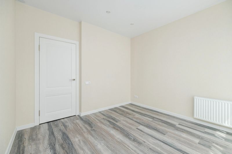 Bright, empty room showcasing freshly painted walls in neutral tones, hardwood flooring, and natural light from multiple sources. Ideal for various decor styles.