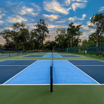 Empty pickleball courts under a vibrant blue sky with scattered clouds.