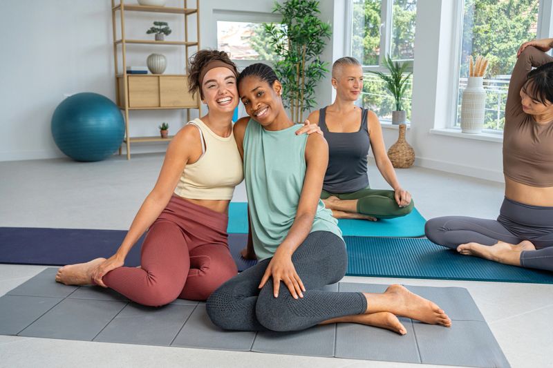 Four women enjoying a yoga session in a serene and well-lit studio space, radiating friendship and wellness. The scene emphasizes camaraderie, physical activity, and mindfulness in a shared environment.