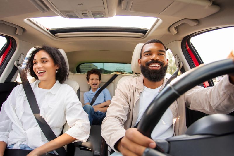 Excited African American family driving car and chatting, having pleasant conversation during ride, parents and son enjoying road trip on vacation
