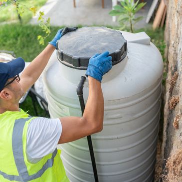 Worker in safety vest handling a large water tank outdoors.