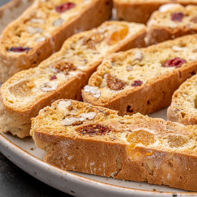 Italian Almond Biscotti biscuits in a rustic home made pottery bowl. Studded with almonds and cranberries, these twice-baked treats are aromatic and inviting. Ideal.