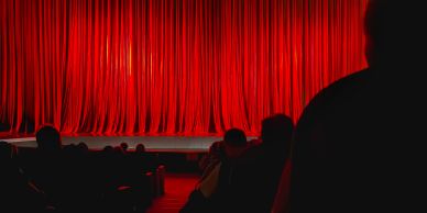 Auditorium with red curtains and seated audience.
