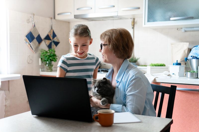 Family using laptop at home. Working mother and daughter. Technology lifestyle, distance education. Woman, child and cat have fun together. Middle school acceptance, back to school allowance, budget.