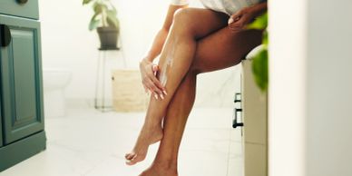 Person applying lotion on their legs in a bright bathroom.