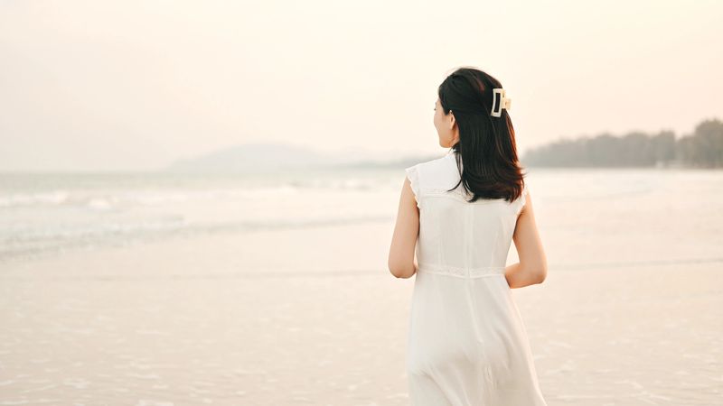 Gen Z woman using her phone share her experiences travel in asia on a sunlit beach, enjoy fresh ocean air shared joyful moment The rolling waves, bright sky, and tropical scenery capture the essence of freedom and relaxation.