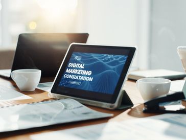Tablet displaying digital marketing consultation on a wooden office desk with laptops and coffee cups.