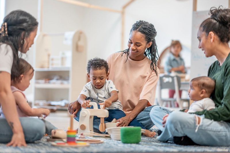 Parents and toddlers interact in a lively learning environment fostering engagement, collaboration, and creativity. Adults teach and nurture children through play, building social and educational skills in a diverse community setting.