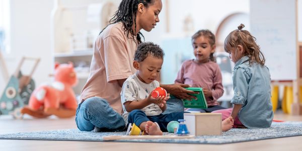 Teacher engaging toddlers in playful learning with toys in a bright classroom.