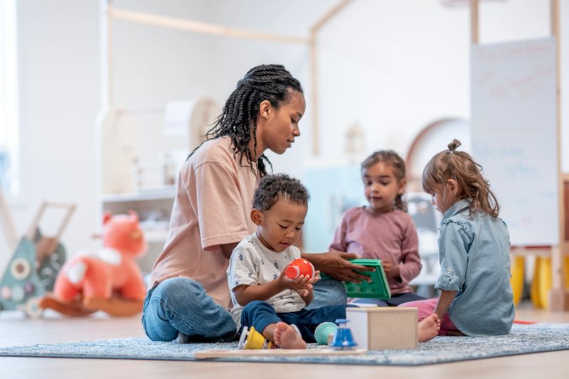 A diverse group of young children learning with a teacher in a colorful playroom, fostering exploration, creativity, and teamwork. The scene emphasizes active education, guided play, and engagement in an engaging preschool setting.