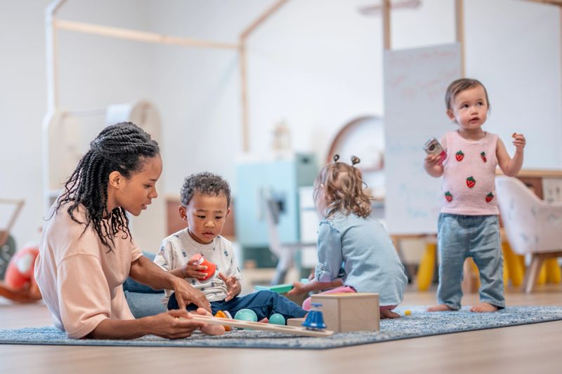 A caring teacher assists young children of diverse backgrounds in a colorful learning environment, promoting creativity and collaboration. The atmosphere highlights early childhood development and positive social interaction.