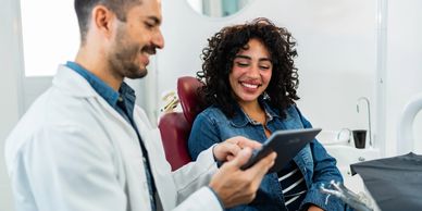 Dentist showing information to a smiling patient on a digital tablet.