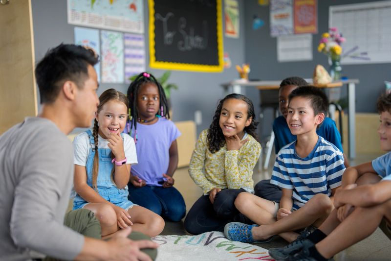 A teacher engages a group of diverse children in a classroom setting, fostering interaction and inclusion. The students display curiosity and enjoyment, creating a positive educational environment.