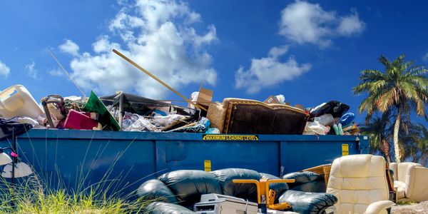 Overfilled dumpster with discarded furniture and household items under a blue sky.