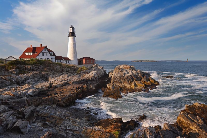 Portland Head Light in late afternoon surrounded by with dramatic waves and cliffs, Maine, USA