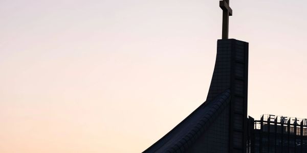 Silhouette of a modern church building with a large cross at sunset.