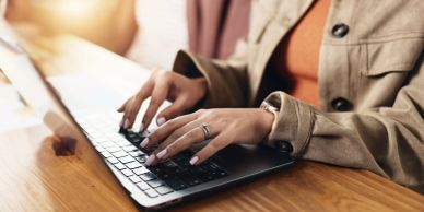Person typing on laptop at wooden table.