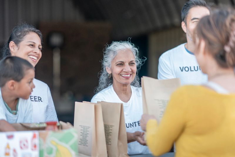 Volunteers interacting warmly while distributing packaged food to people in need during a community program, highlighting teamwork, generosity, and diversity among participants.