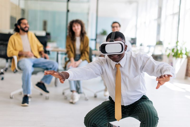 A group of coworkers enjoying their work break by using a VR headset, sharing laughter and creating a lively atmosphere in the office.