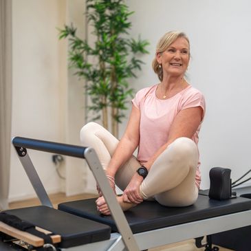 A woman stretching on Pilates reformer machine in a bright room.