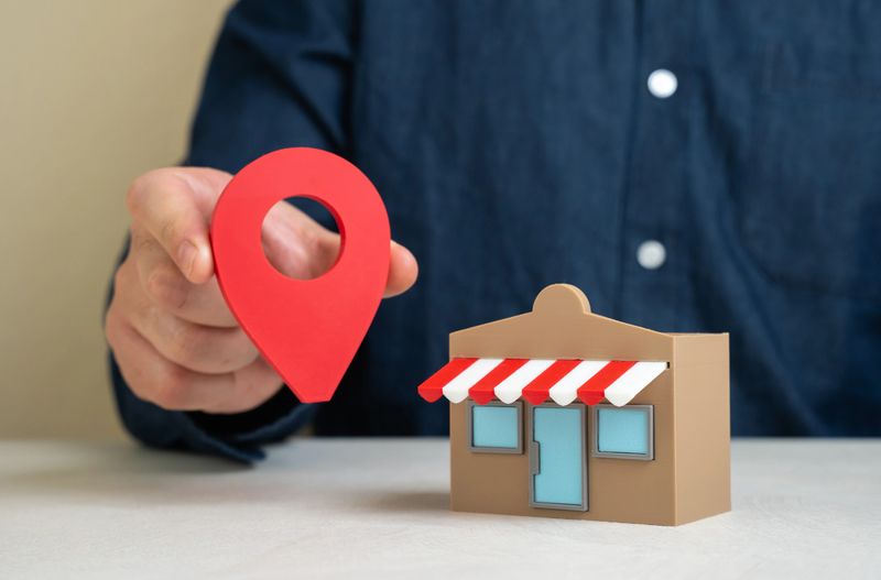 A man holds a geolocation pin near a store. Convenient location and high customer traffic. Business visibility. Role of location in boosting sales, branding, and competitive edge.