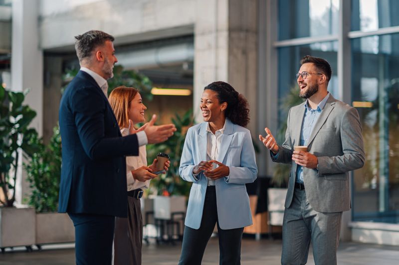 Four business people are enjoying a coffee break, talking and laughing together in a modern office building