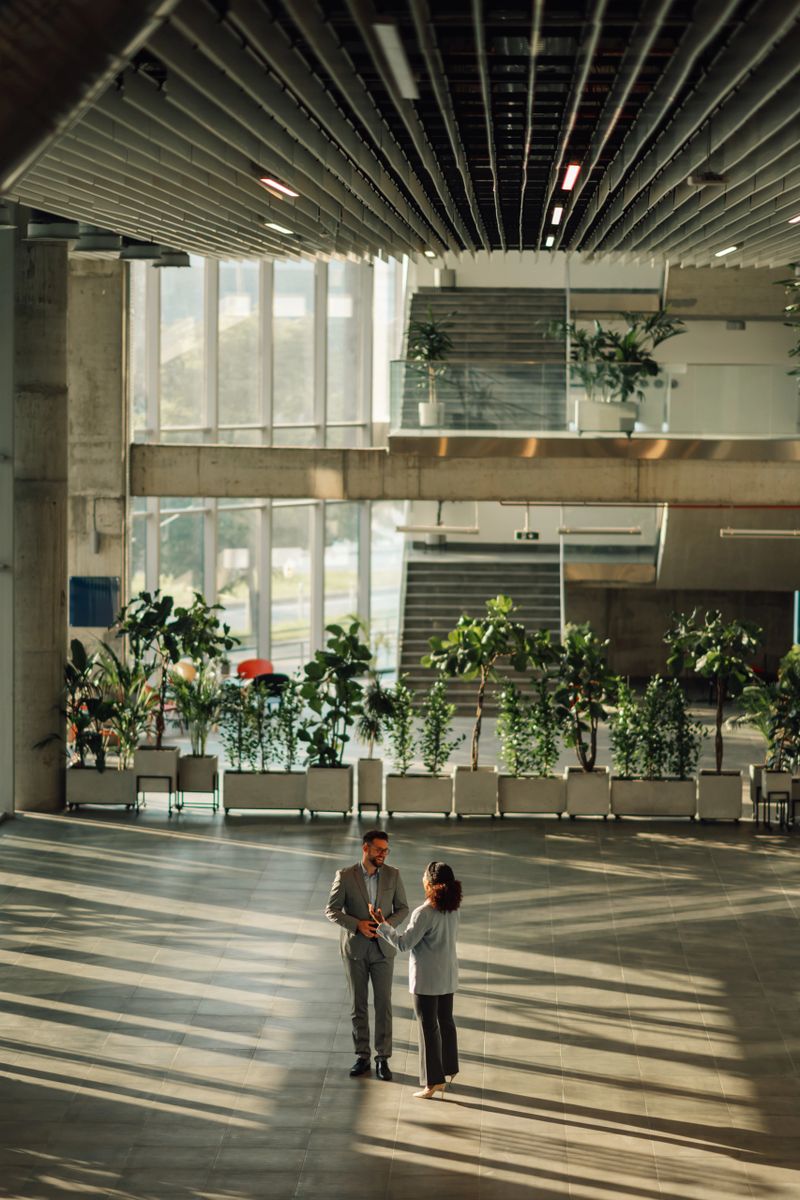 Two businesspeople standing in a bright, modern office lobby, engaging in conversation and showcasing a collaborative atmosphere