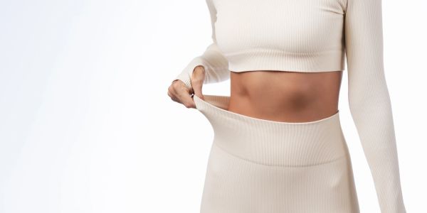 Person showing loose waistband on beige outfit, indicating weight loss.