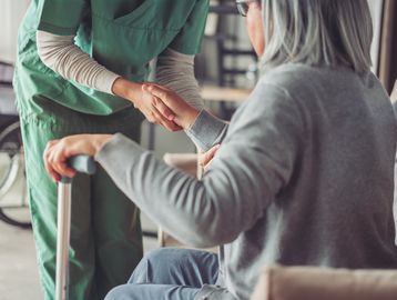 A caregiver holds the hand of an elderly person using a walker.