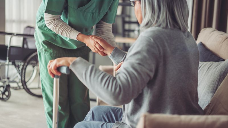 The nurse is helping the old patient with a cane