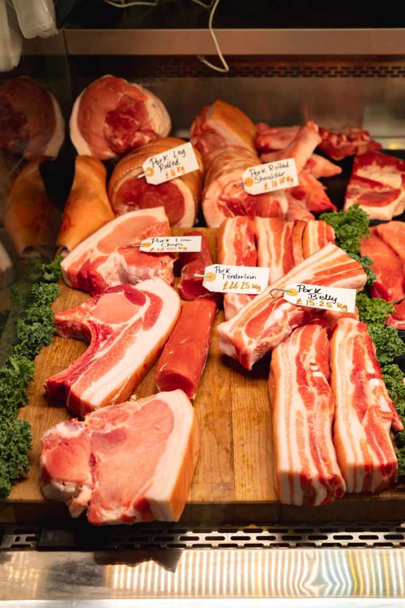 Various cuts of fresh pork are displayed on a wooden cutting board, ready for sale at borough market in london
