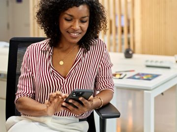 Woman smiling while using smartphone in a modern office.