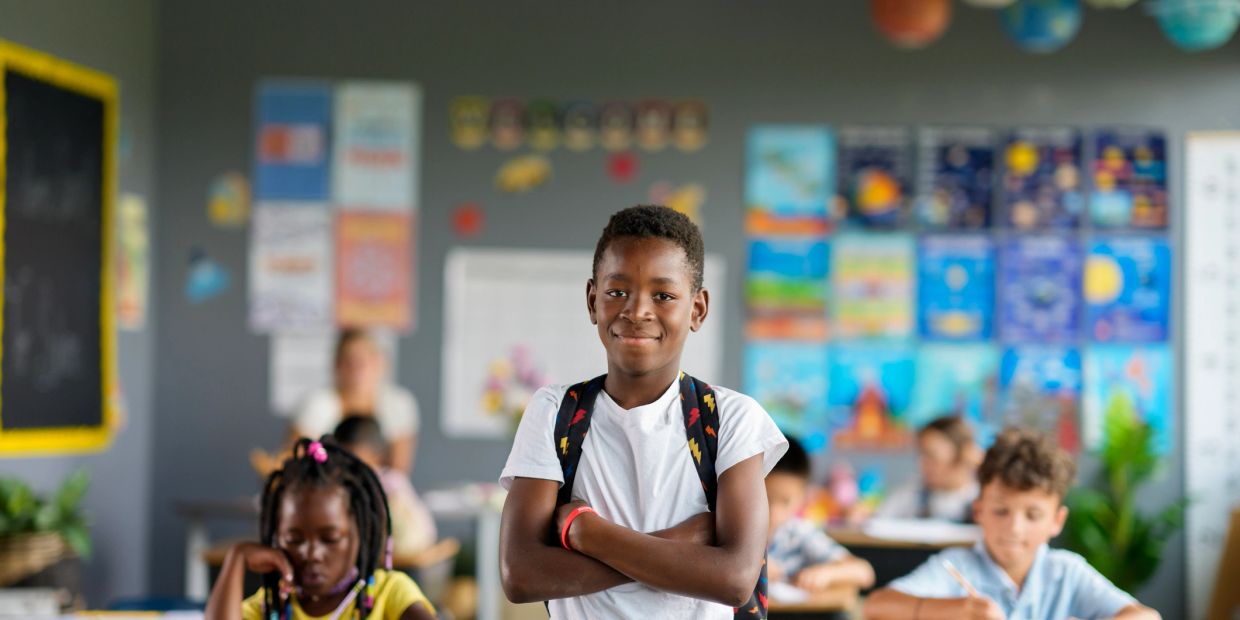 Confident boy standing with arms crossed in colorful classroom.