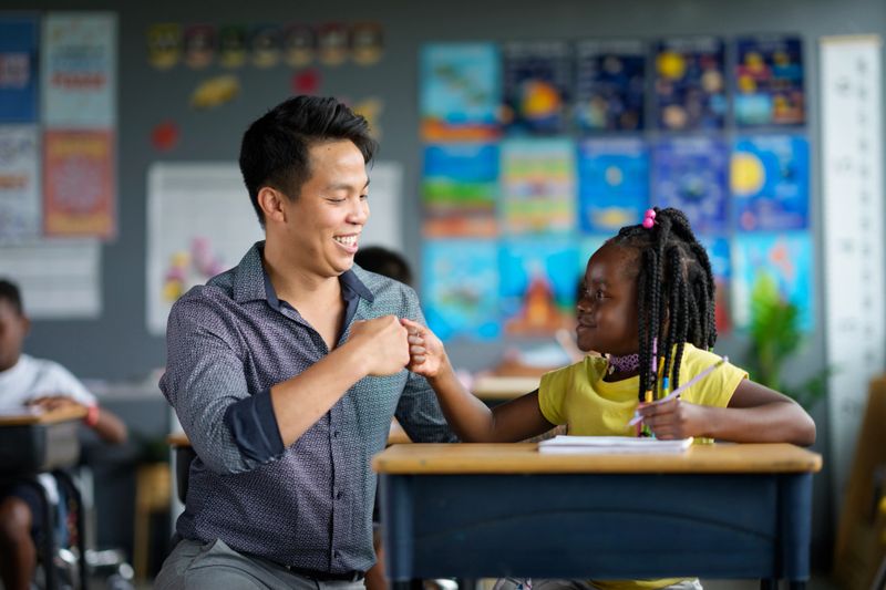 A young girl eagerly learning from her attentive teacher in a vibrant classroom setting. The atmosphere promotes education, understanding, and connection between students and educators, fostering an inclusive and motivating environment.