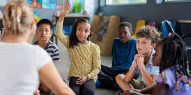 A girl raises her hand in a classroom setting.