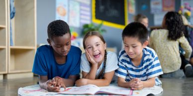 Three kids reading together on the floor in a classroom.
