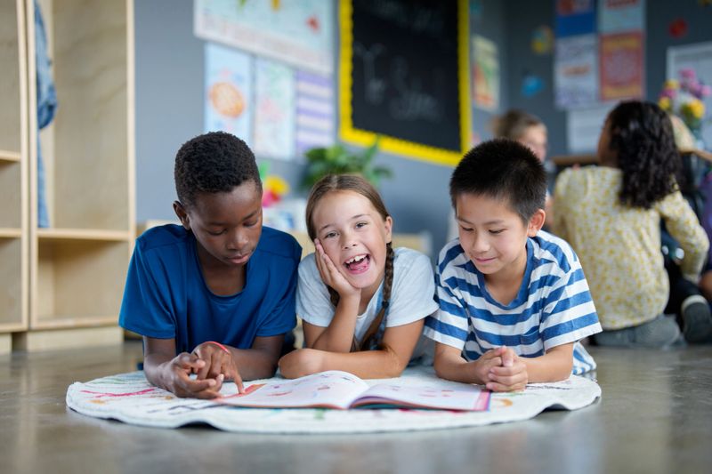 Young kids engaging in reading activities on the floor of a colorful classroom setting, illustrating friendship, diversity, and learning in a supportive educational environment.