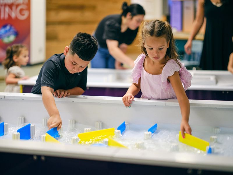 Children playing with an interactive water table exhibit in a children’s museum.