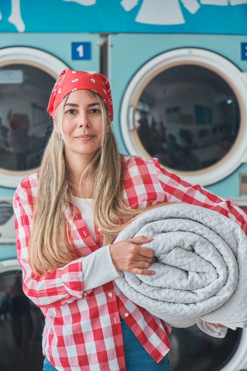 Laundromat worker holding a rolled up blanket, preparing to load it into a washing machine