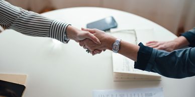 Two people shaking hands over a table with documents and phones.