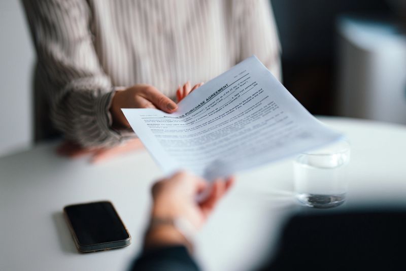 Close-up focus on a professional handing over an official document during a meeting. Dedicated, collaborative, and professional atmosphere conveying business negotiations and cooperation.