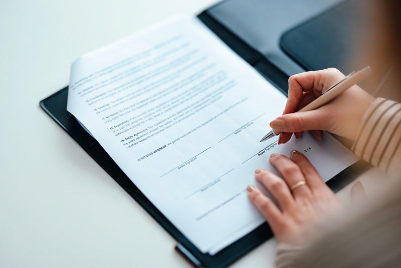 A professional individual signs an official document in an office, highlighting themes of business, agreement, and professionalism. The close-up captures formality and significance in corporate or legal contexts.
