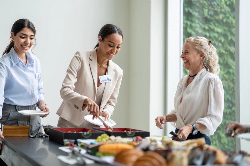 Group of professional women at a business networking event, engaging in conversation and enjoying refreshments in a lively and casual setting. Connection and camaraderie are emphasized in a welcoming environment.