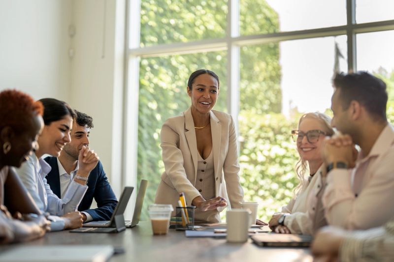 A team of professionals gathers in a well-lit office space, engaging in a productive business meeting. The image showcases diversity and teamwork in a corporate environment with laptops and coffee on the table.