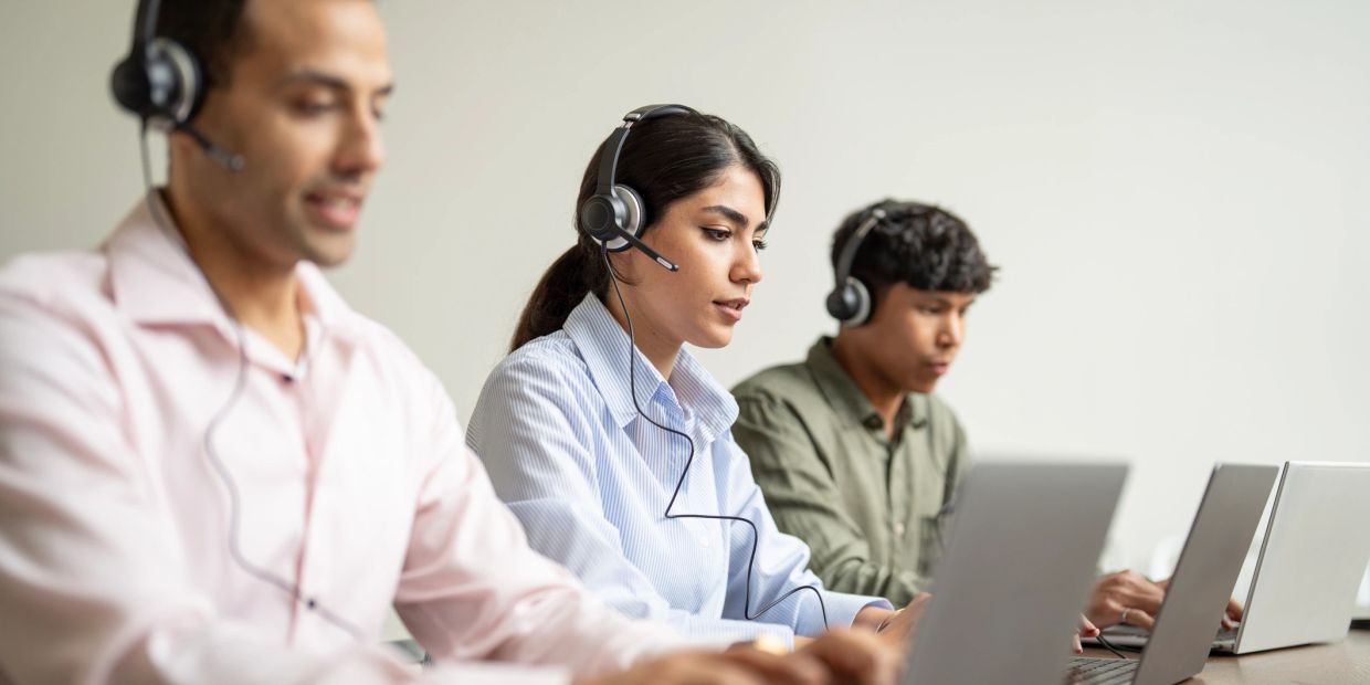 Three call center agents working attentively with headsets and laptops.