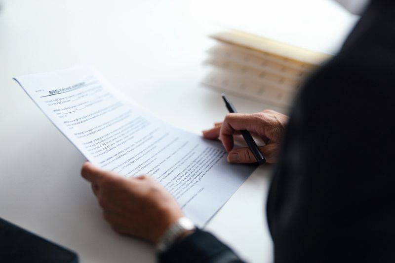 A professional reviewing an official document with a pen in hand, symbolizing business and financial evaluation. Set in a modern office environment with clean and organized surroundings.