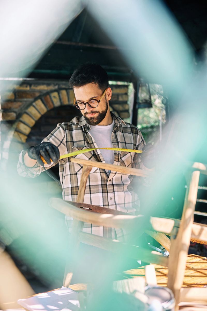 A focused craftsman repairs wooden furniture in a home workshop with precision tools, showcasing creativity and skilled woodworking techniques.