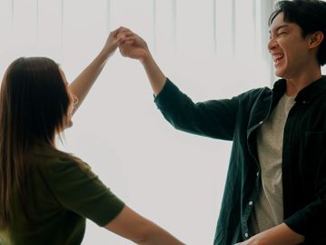 Two people joyfully holding hands indoors.