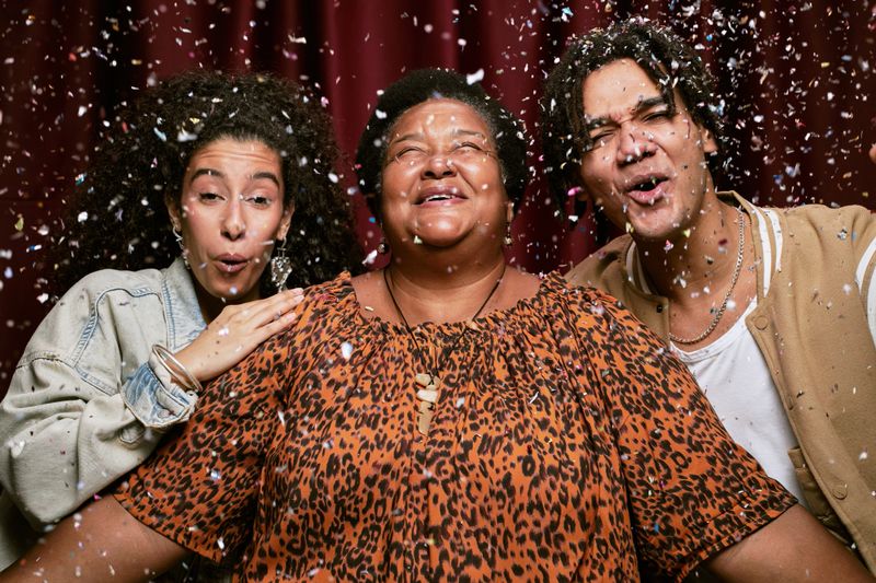 Portrait of middle aged Black woman smiling with two young adults, biracial woman and man, standing close together in photo booth with confetti falling